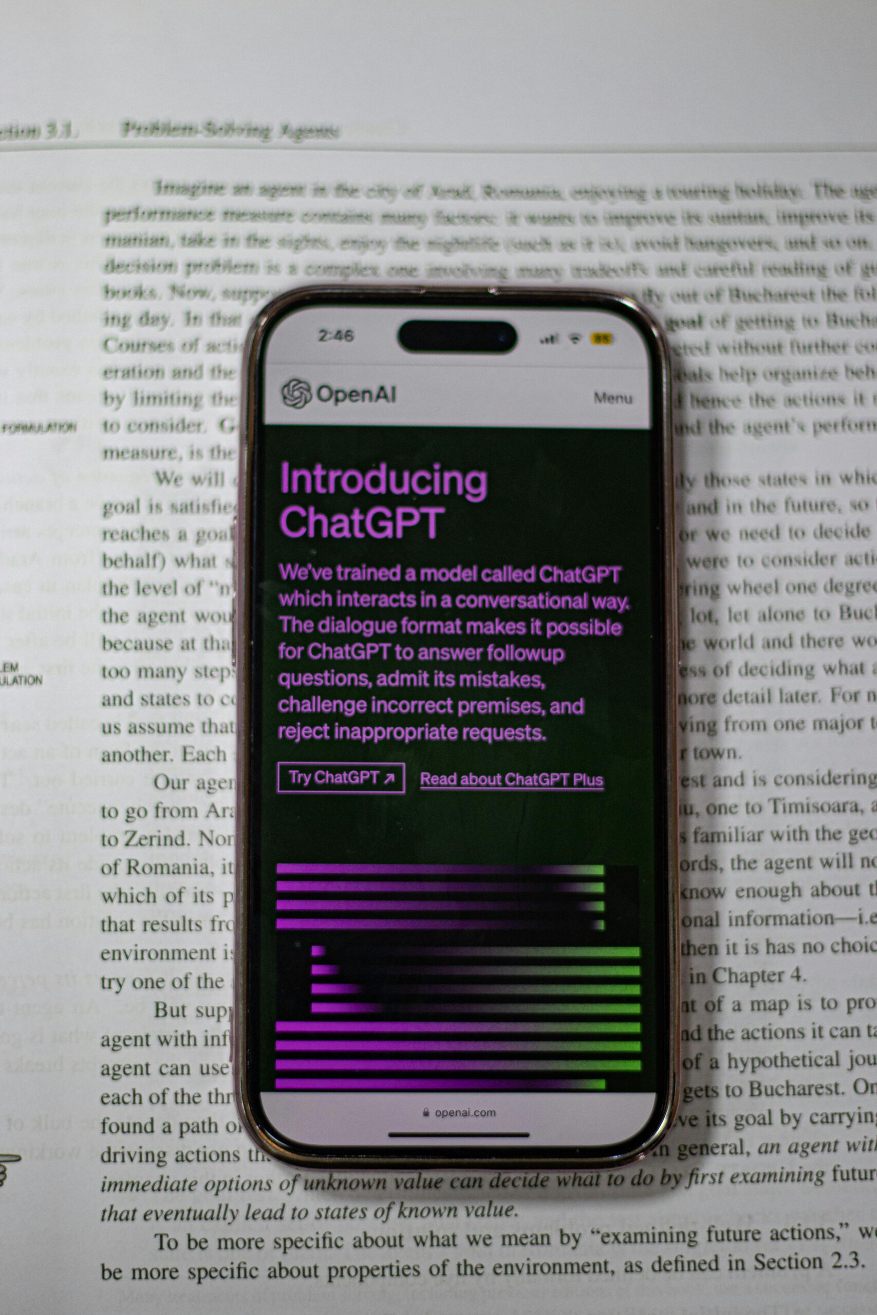 A mobile phone displaying ChatGPT is placed on top of an open book.