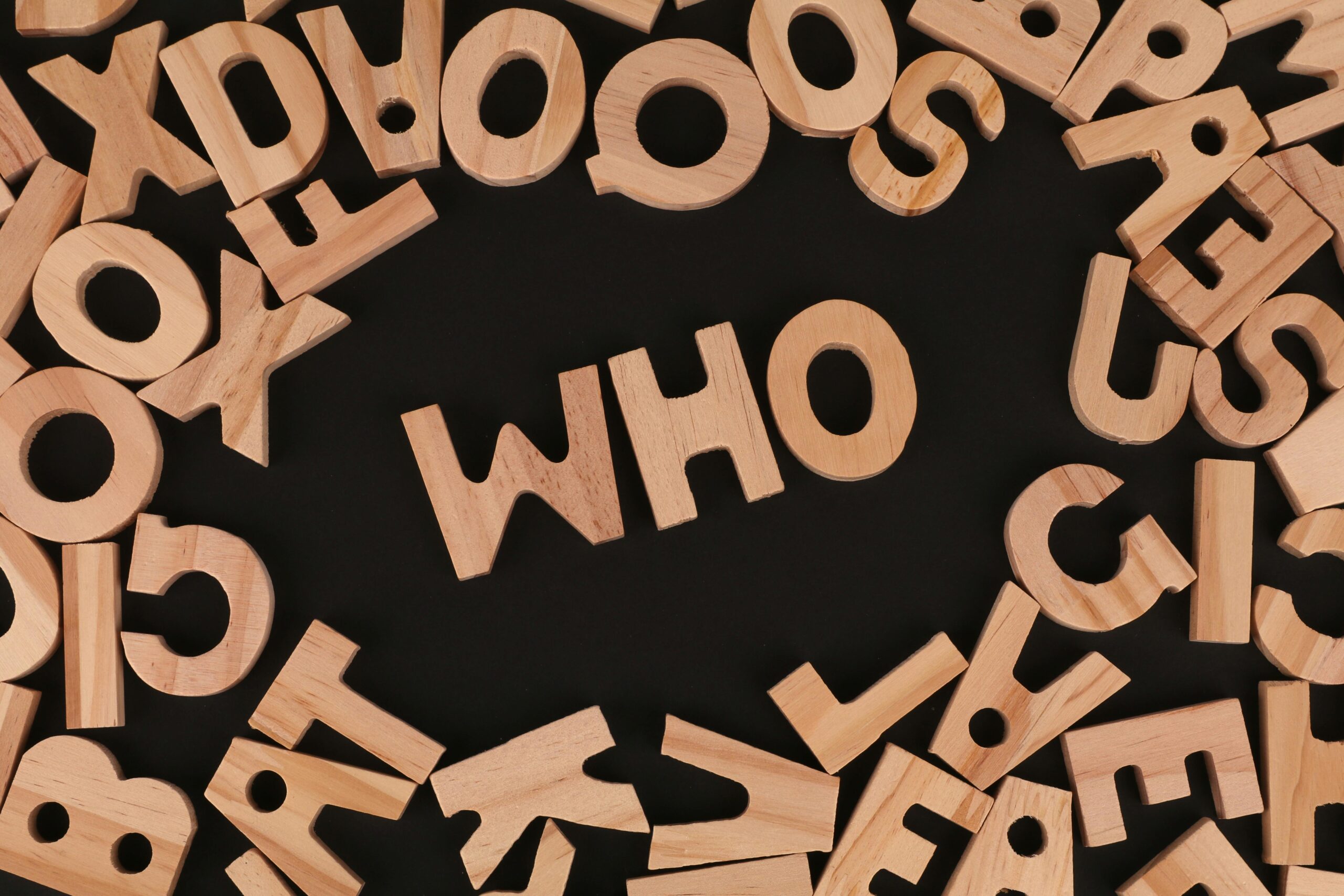 Wooden alphabet letters arranged to spell 'Who' on a black surface, creative message concept.