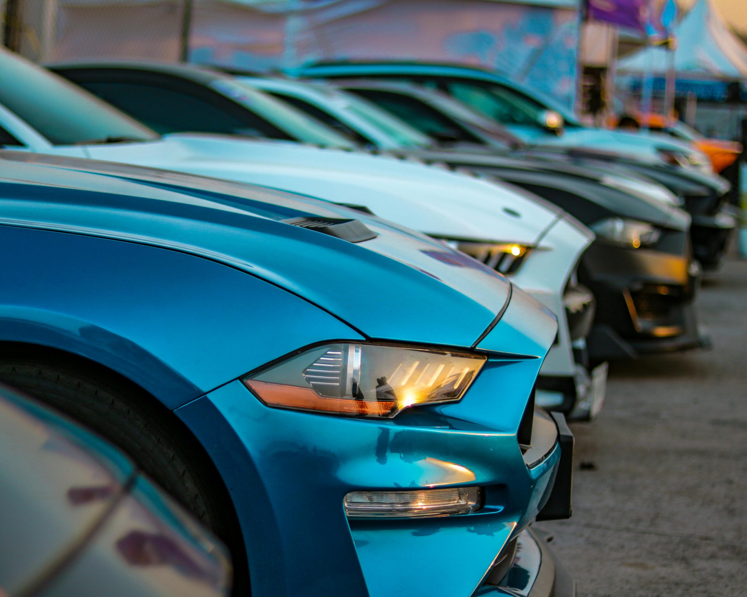 A close-up view of colorful sports cars lined up in an outdoor auto show, showcasing their sleek designs.